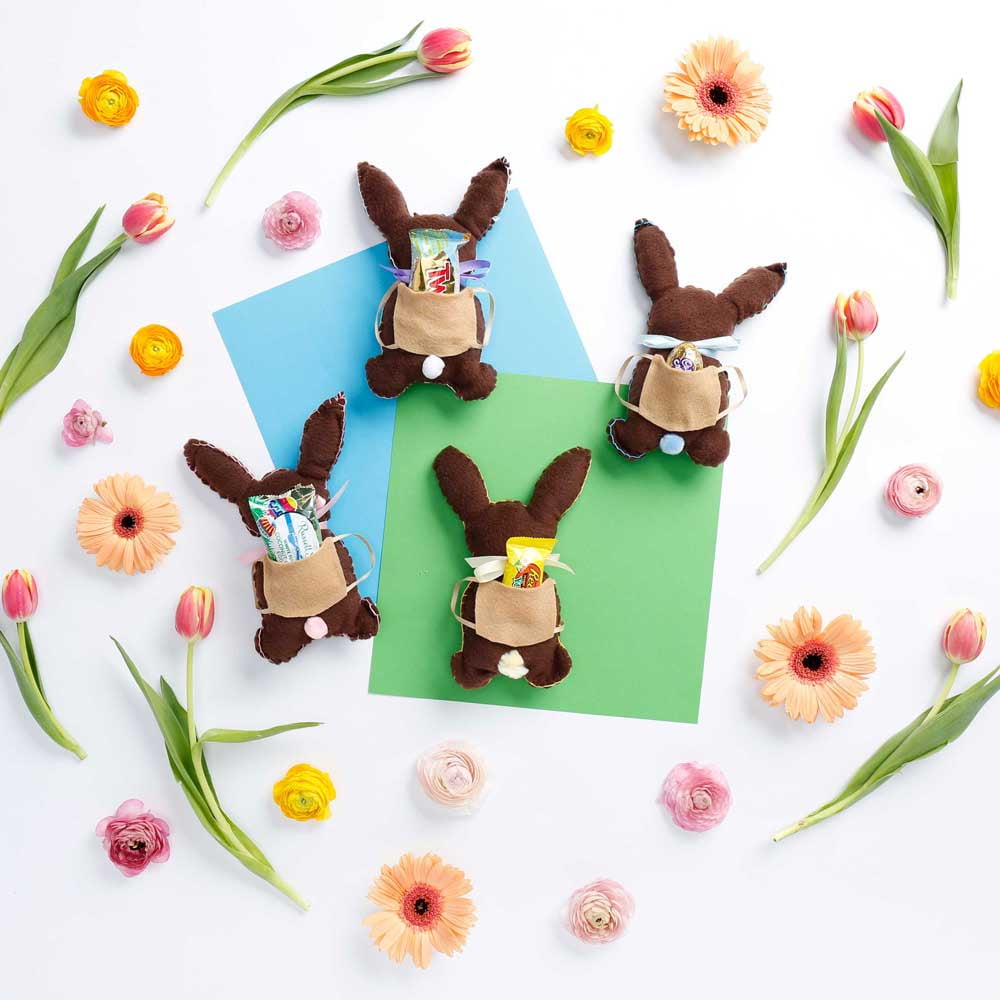 4 bunnies with candy in their backpacks surrounded by spring flowers