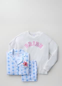 A blue printed pajama set and a white sweatshirt with “bride” in pink letters are layered on top of one another.