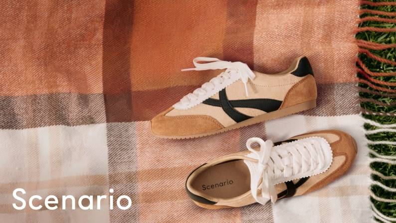 Pair of tan and cream suede sneakers with black accents displayed on a plaid picnic blanket.