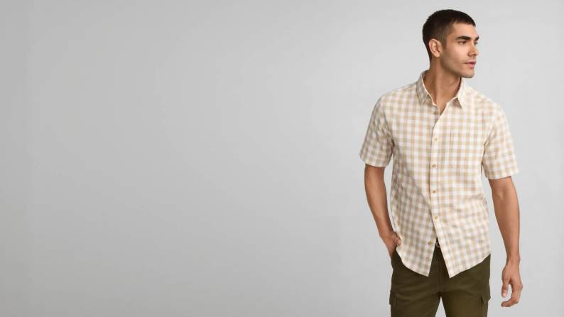 Man wearing a short-sleeved button-up poplin shirt in a sesame seed colored gingham print.