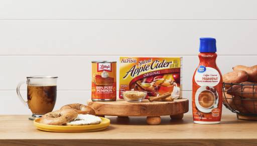 Libby’s one hundred percent pure pumpkin, Alpine spiced apple cider, Great Value hazelnut creamer next to sweet potatoes, bagels, coffee and cinnamon.