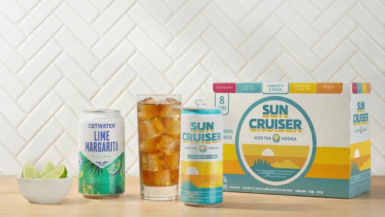 A bowl of lime wedges, a can of Cutwater lime margarita, a glass, can, and variety pack of Sun Cruiser iced tea vodka drinks.