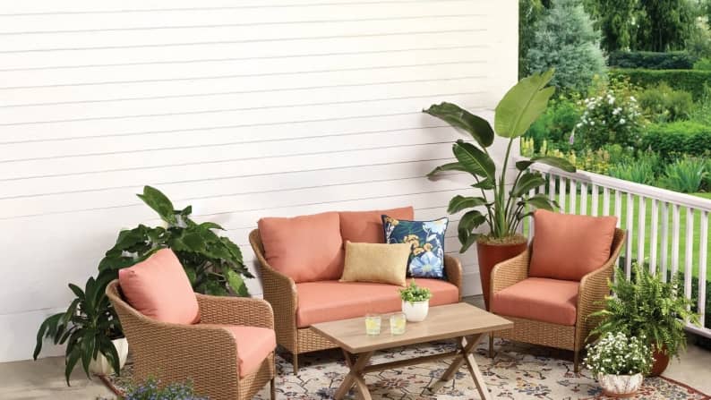 Pink and tan patio furniture on a back porch, surrounde dby green plants.