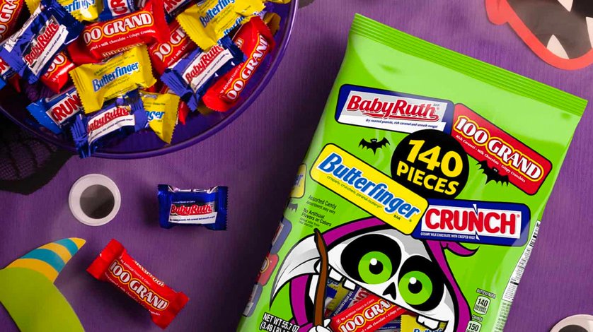 An assortment of fun-size, trick-or-treat candies in a bowl, set beside a bag filled with the very same candies.