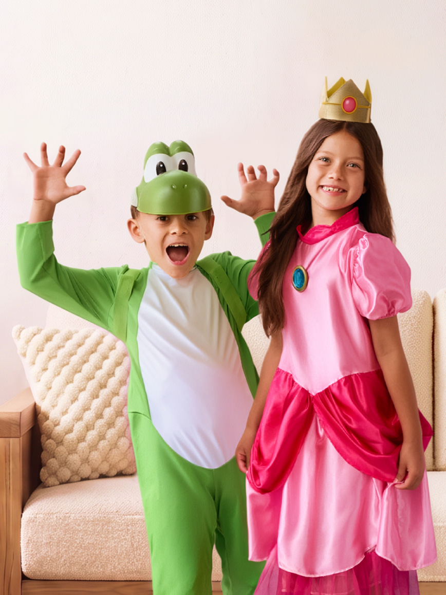 Two children wear a green dinosaur costume and a pink princess costume indoors.