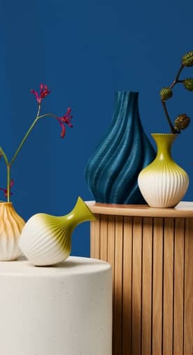 Two pedestals are next to each other. Both feature vases in various textures and colors. Botanical elements are inside two of them.