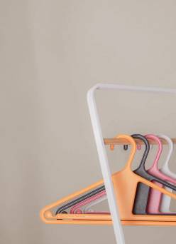 Closet hangers in multiple colors rest on an open rack.