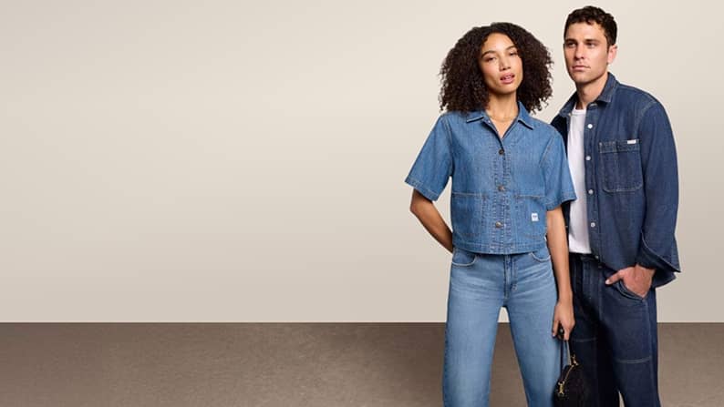 A woman and a man in denim shirts and jeans are pictured on a beige backdrop.