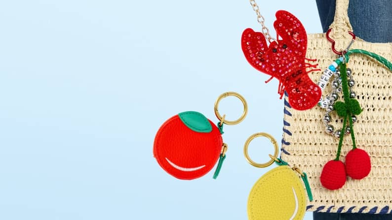 Woven tote decorated with colorful fruit and novelty bag charms against a light blue background.