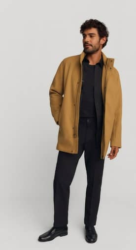 A man is wearing a caramel jacket, a black shirt, black pants and black shoes.