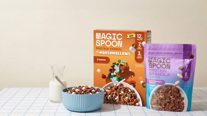 A box of Magic Spoon cereal, a package of Magic Spoon granola, a glass of milk, and a bowl of cereal with a spoon in it.