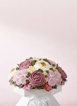 A cardboard stand holding a cupcake bouquet that’s decorated to look like various pink, mauve, and white flowers with green leaves.