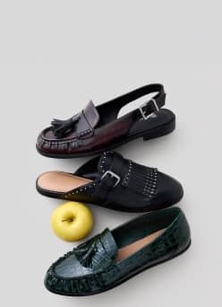 Three womens loafers with tassel and buckle details arranged with a yellow apple.