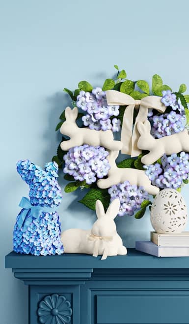 Bunny-shaped artificial flower arrangement, wreath with leaping bunnies as well as bunny and egg ornaments.