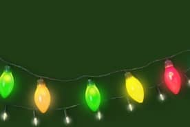 Image shows a close-up of a mantel decorated with Christmas house figurines, reindeer and large multi-colored Christmas lights.