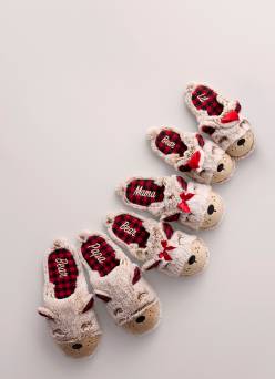 Three pairs of matching reindeer slippers are pictured on a beige backdrop.