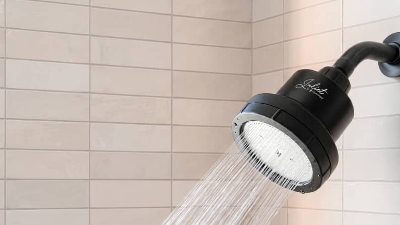 Black Juliet filtered showerhead with water running in a tiled shower.