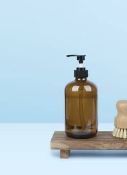 Small wood tray pedestal holding hand soap dispenser and shaving brush.