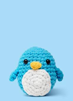 A crocheted Woobles blue and white knit penguin with a yellow beak on a light blue background.
