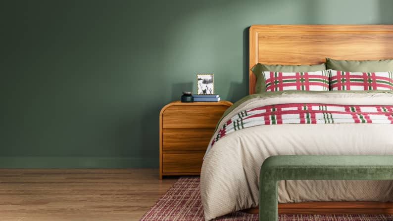 A wooden bed with plaid bedding is shown with a matching nightstand against a sage wall.