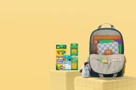 A backpack filled with and surrounded by school supplies and a plush penguin charm.