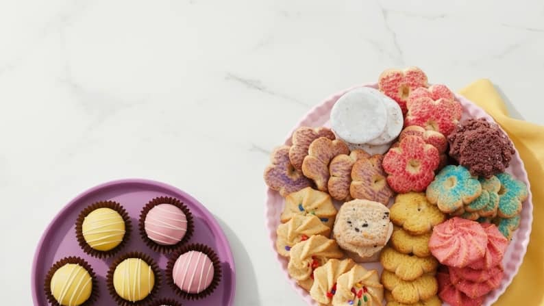 A plate of yellow and pink cake poppers next to a platter of cookies, including shortbread cookies in various shapes and flavors.