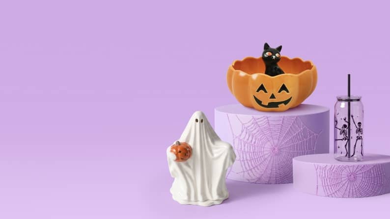 A jack-o'-lantern bowl with a black cat inside, a ceramic ghost and a skeleton glass sit on purple pedestals.