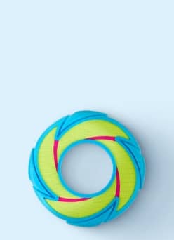 Round blue and green dog toy with pink accents on a plain surface.