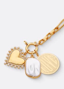 A heart, faux-pearl and coin charm are pictured on a gold chain on a light grey backdrop.