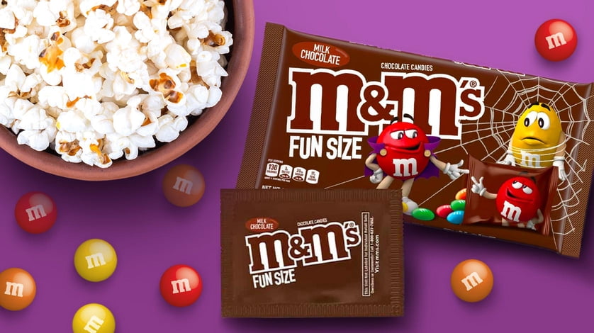 Packages of fun size M&M’s candies, set beside a bowl filled with popcorn.