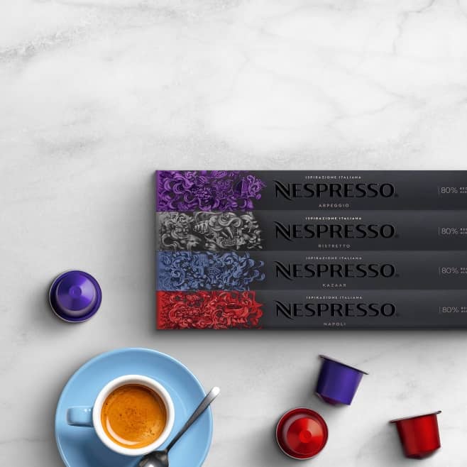 Four packages of Nespresso coffee capsules are shown next to a cup of coffee on a saucer with a spoon next to it.