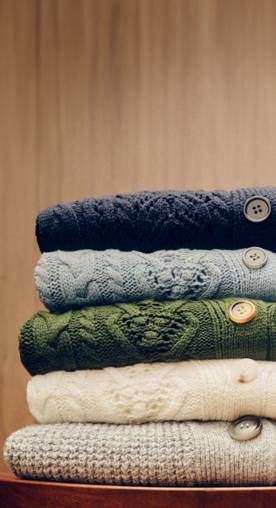 A stack of four colorful cardigans is pictured against a brown wood backdrop.