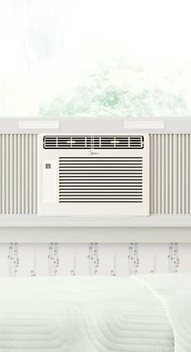A white air conditioner in a window overlooking green trees.