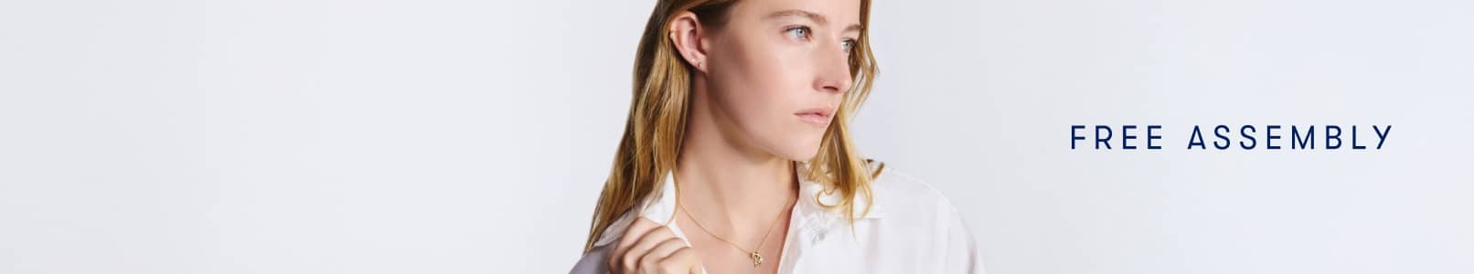 A woman wearing a white blouse and delicate gold necklace, looking to the side against a light background.