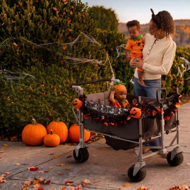 A mother holds a child in a Fred Flinstone costume next to a baby dressed as a pumpkin in a decorated stroller.