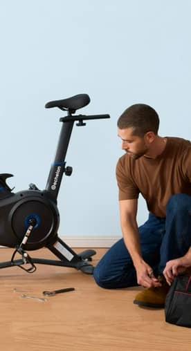 An image of a person kneeling in front of an exercise bike.