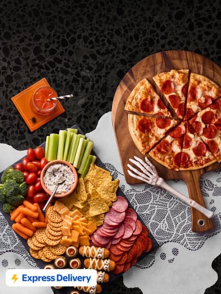 Express Delivery badge. Pepperoni pizza and snack platter with vegetables, crackers, chips, deli meats, cheese rolls and dip on lace tablecloth.