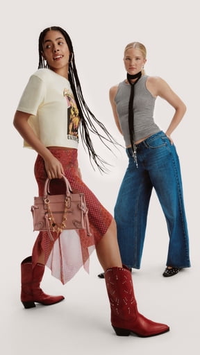 Two women wearing a cream graphic tee with a red skirt and boots, and a gray sleeveless knit top with wide leg jeans.