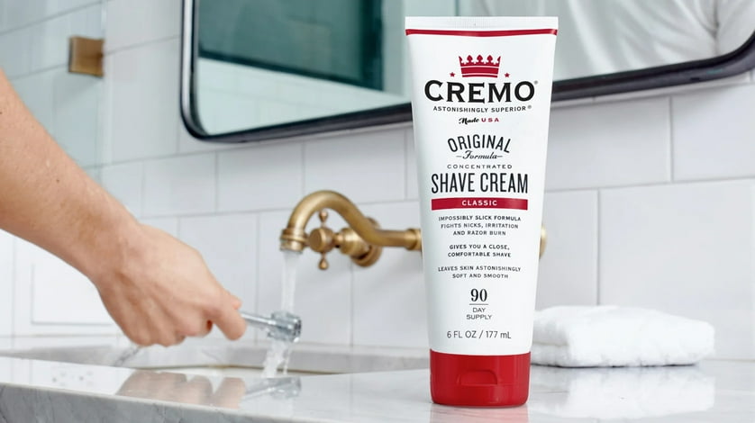 Cremo shave cream on a bathroom counter near someone preparing their razor