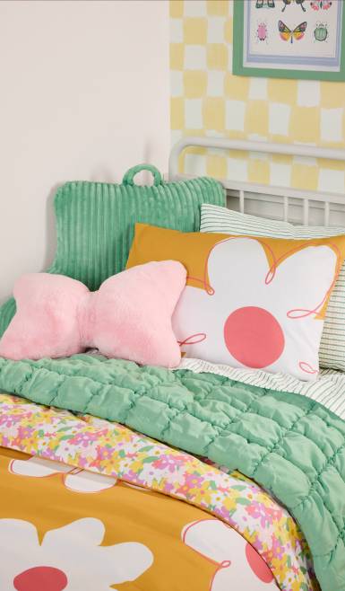 Floral and daisy-patterned bedding with a pink bow-shaped pillow and a green backrest pillow. Reads: Daisy dreams. From eleven eighty-four.