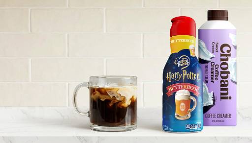 A glass mug of black coffee with coffee creamer swirl is pictured next to a bottle of Coffeemate Harry Potter creamer and Chobani sweet cream.