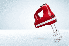 Image shows an empire red KitchenAid hand mixer with three speeds on a light blue background.