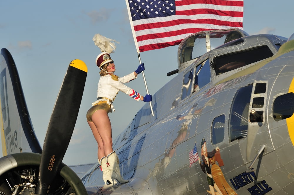 1940s style majorette pin-up girl on a B-17 bomber with an American flag Canvas Art - Christian KiefferStocktrek Images (35 x 23)
