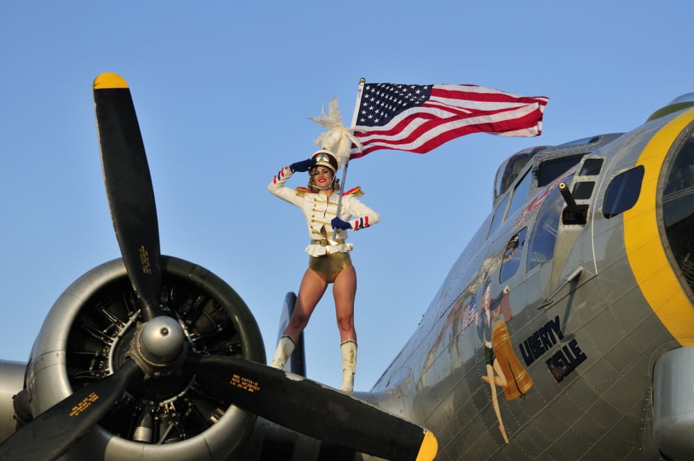 1940s style majorette pin-up girl on a B-17 bomber with an American flag Canvas Art - Christian KiefferStocktrek Images (35 x 23)