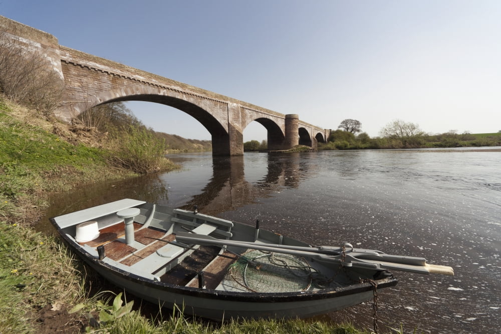 A Boat Along The Shoreline Beside A Bridge In River Tweed Scottish Borders Scotland Canvas Art - John Short Design Pics (19 x 12)