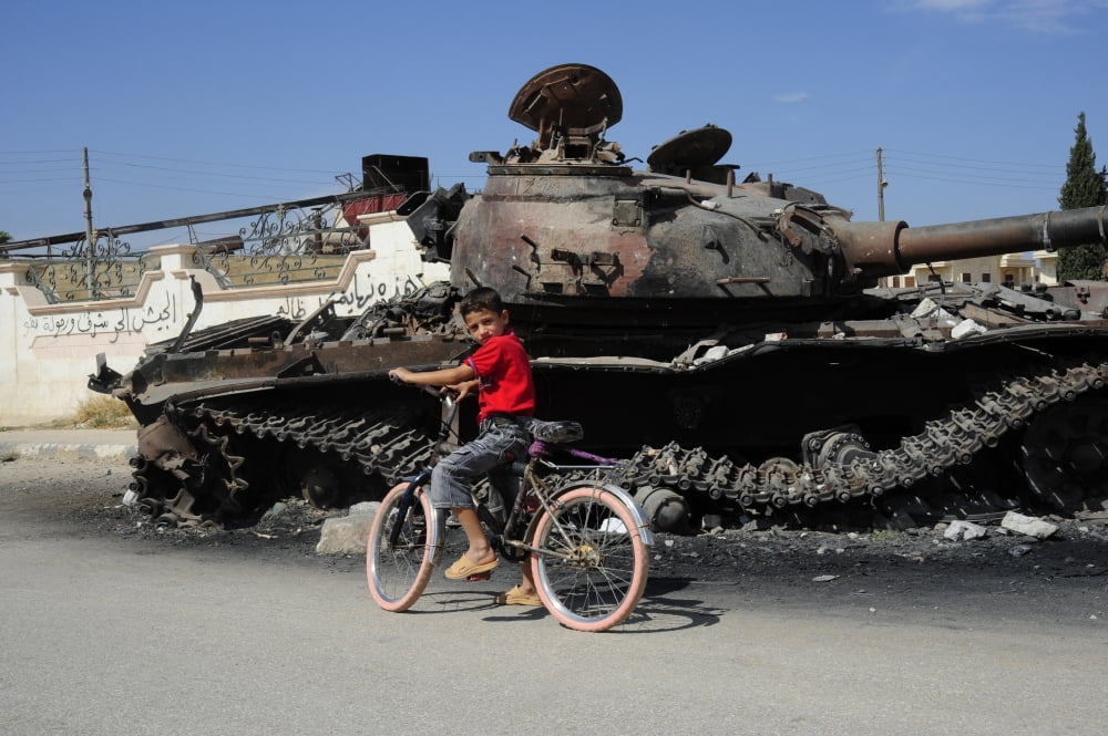 A Syrian boy on his bicycle in front of a destroyed T-72 battle tank Canvas Art - Andrew ChittockStocktrek Images (18 x 12)