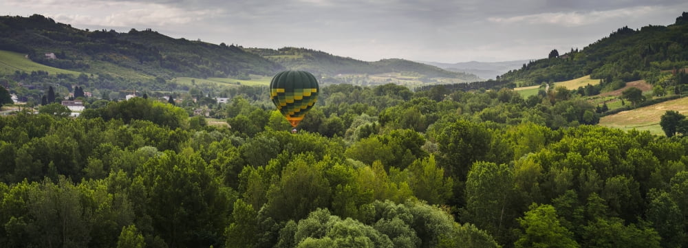 A hot air balloon flies low over a spring valley landscape Tuscany Italy Canvas Art - Brian Guzzetti Design Pics (44 x 16)