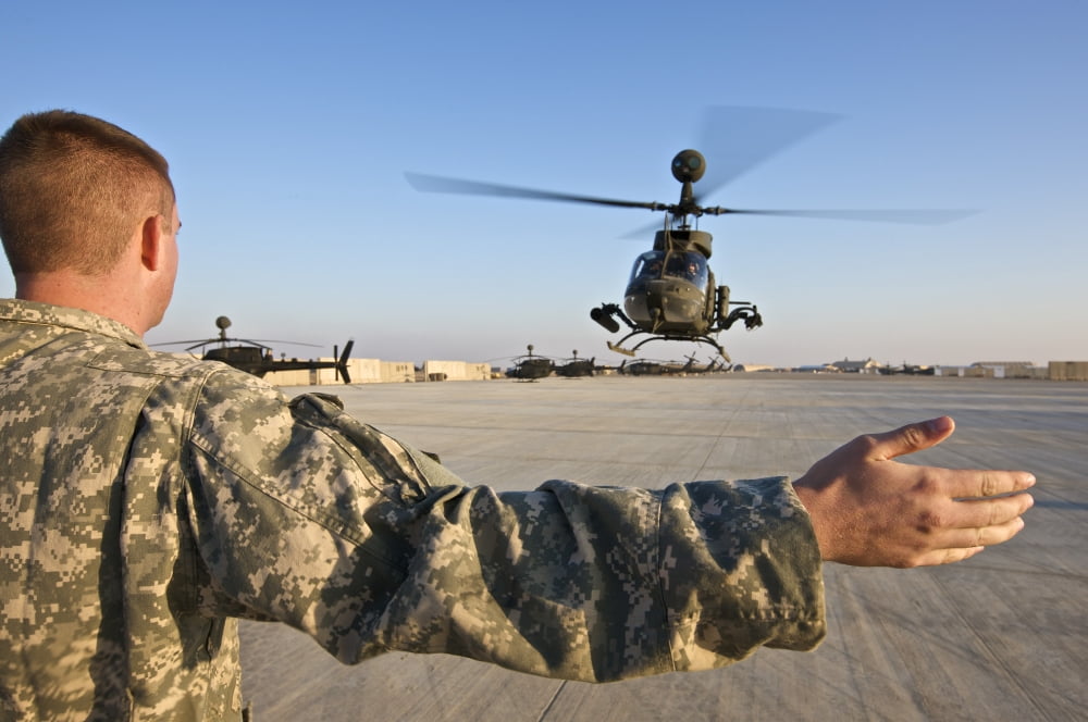 A soldier guides an OH-58D Kiowa helicopter as it lands on a military base Canvas Art - Terry MooreStocktrek Images (18 x 12)