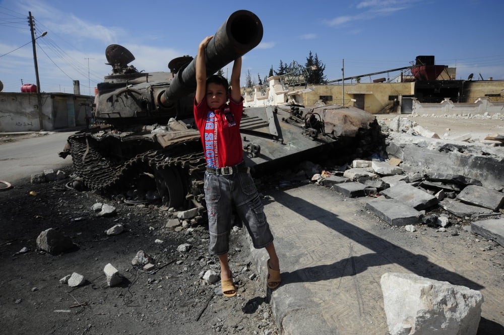 A young Syrian boy plays on the turret of a destroyed T-72 battle tank Canvas Art - Andrew ChittockStocktrek Images (18 x 12)