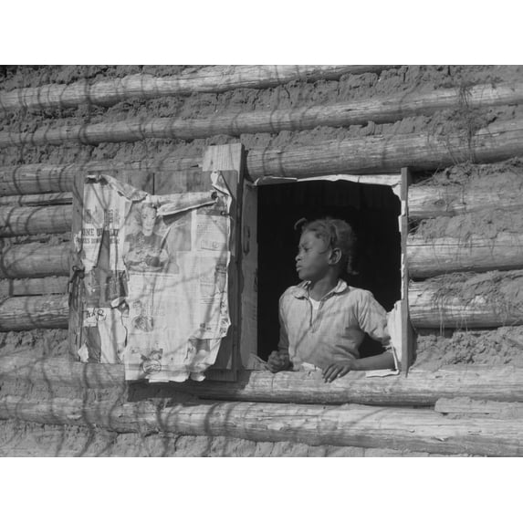 African American Girl Looking Out The Window Of A Plantation Log Cabin Tenants Home. Newspaper Advertisements On The Shutter Beckon From The Larger World Beyond Rural Poverty. April 1937 Photo By